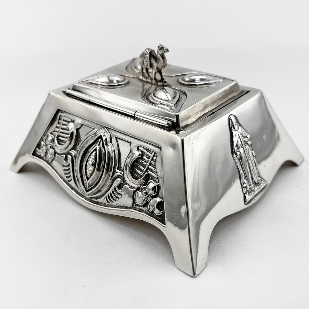 A square sterling silver trinket casket featuring a camel finial on the lid and detailed desert relief panels along the sides. View V