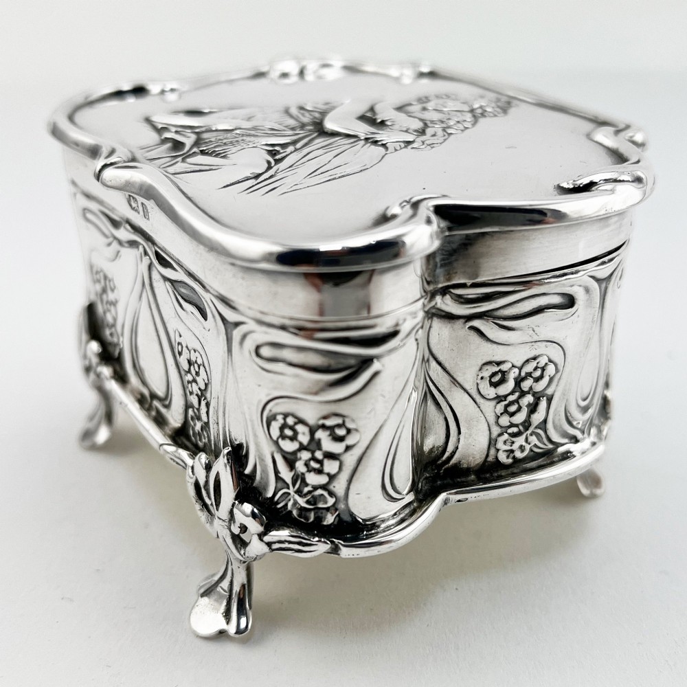 An Edwardian sterling silver trinket box featuring a raised relief depiction of a mother embracing a child on the hinged lid, set on scrolled silver feet. View IV