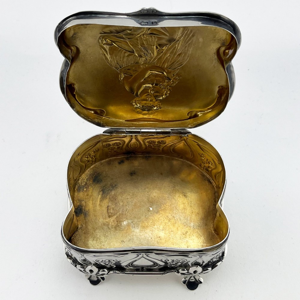 An Edwardian sterling silver trinket box featuring a raised relief depiction of a mother embracing a child on the hinged lid, set on scrolled silver feet. View VI