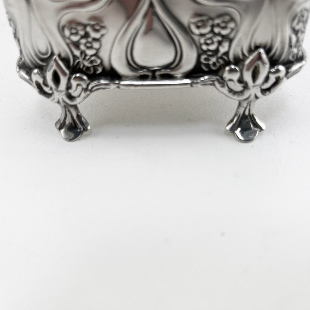 An Edwardian sterling silver trinket box featuring a raised relief depiction of a mother embracing a child on the hinged lid, set on scrolled silver feet. View VII