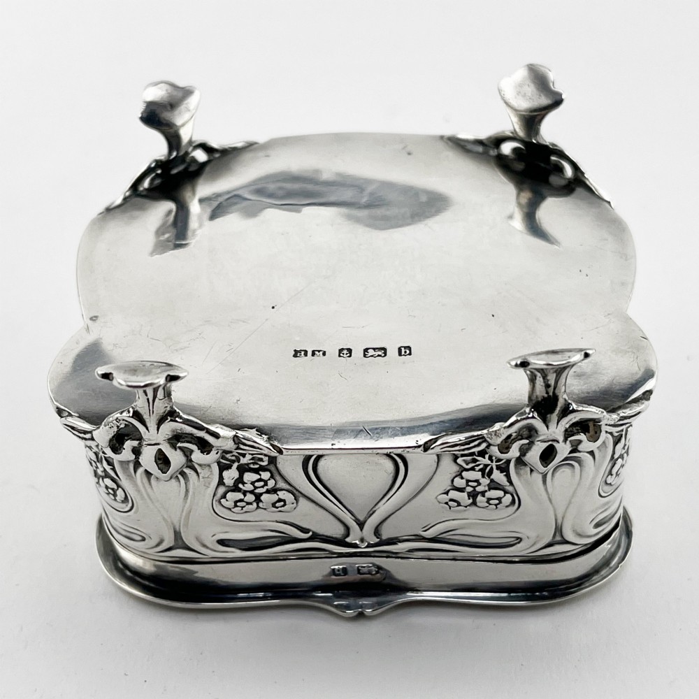 An Edwardian sterling silver trinket box featuring a raised relief depiction of a mother embracing a child on the hinged lid, set on scrolled silver feet. View IX