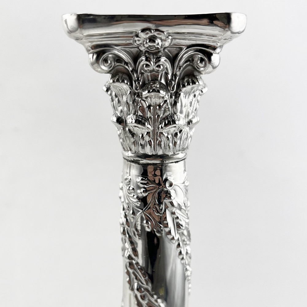 A pair of silver-plated column candlesticks featuring Corinthian capitals, spiral foliate garlands along the shafts, and square stepped bases. View IV