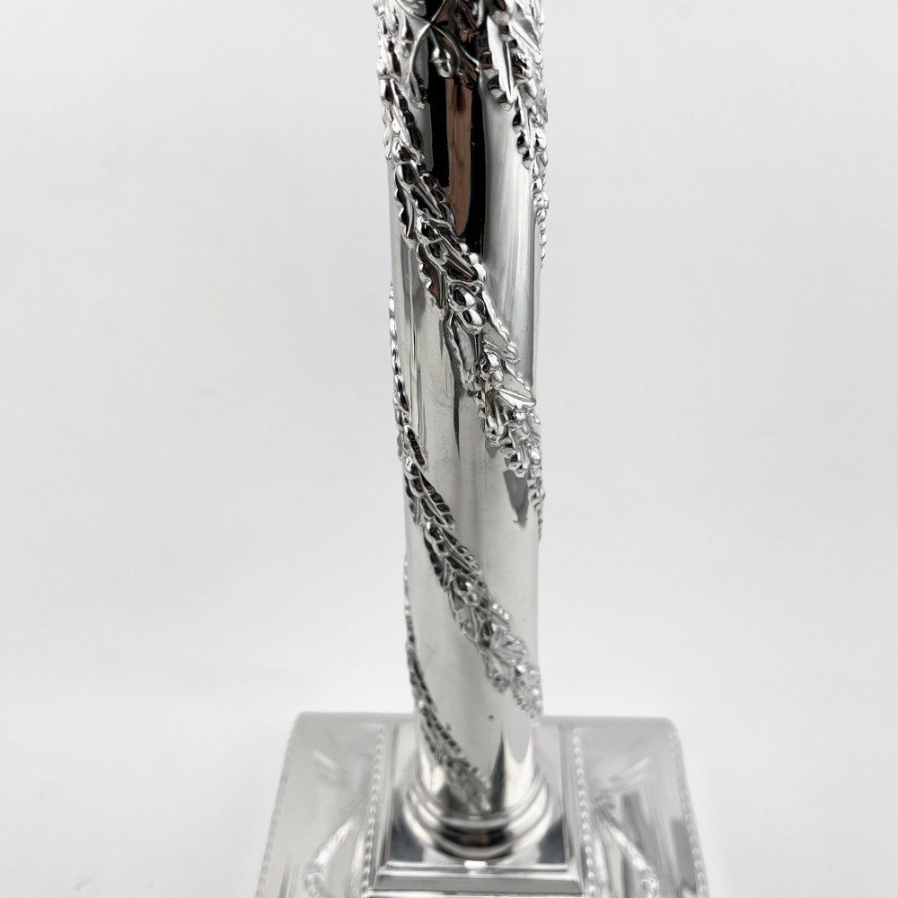 A pair of silver-plated column candlesticks featuring Corinthian capitals, spiral foliate garlands along the shafts, and square stepped bases. View V
