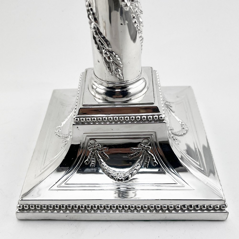 A pair of silver-plated column candlesticks featuring Corinthian capitals, spiral foliate garlands along the shafts, and square stepped bases. View VI