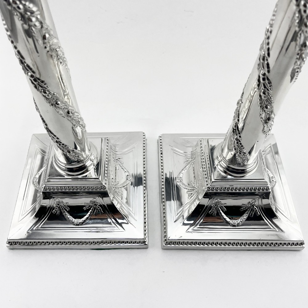 A pair of silver-plated column candlesticks featuring Corinthian capitals, spiral foliate garlands along the shafts, and square stepped bases. View VII