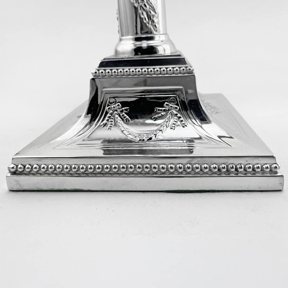 A pair of silver-plated column candlesticks featuring Corinthian capitals, spiral foliate garlands along the shafts, and square stepped bases. View VIII