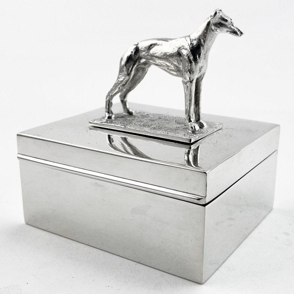 A rectangular silver-plated box featuring a polished finish and a sculpted figure of a standing greyhound attached to the lid.
