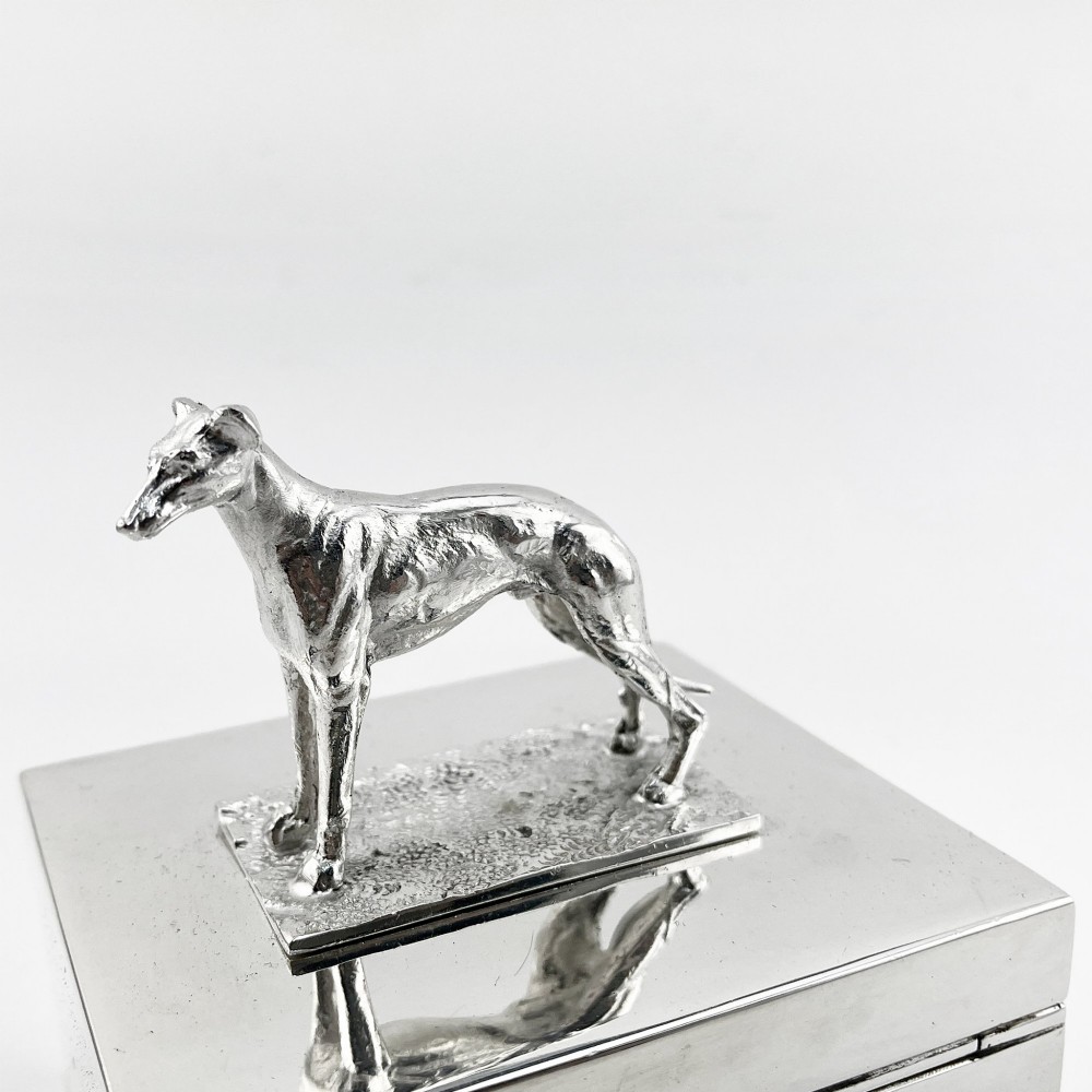 A rectangular silver-plated box featuring a polished finish and a sculpted figure of a standing greyhound attached to the lid. View III