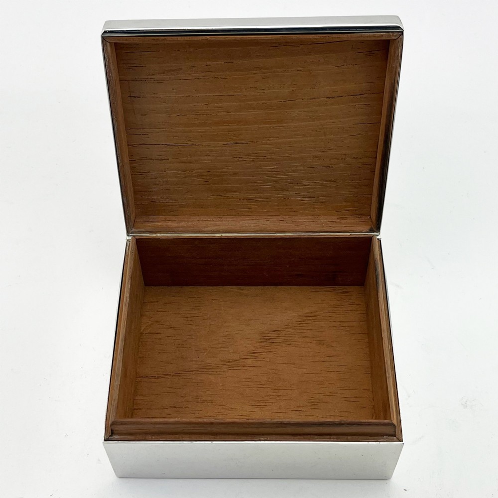 A rectangular silver-plated box featuring a polished finish and a sculpted figure of a standing greyhound attached to the lid. View V