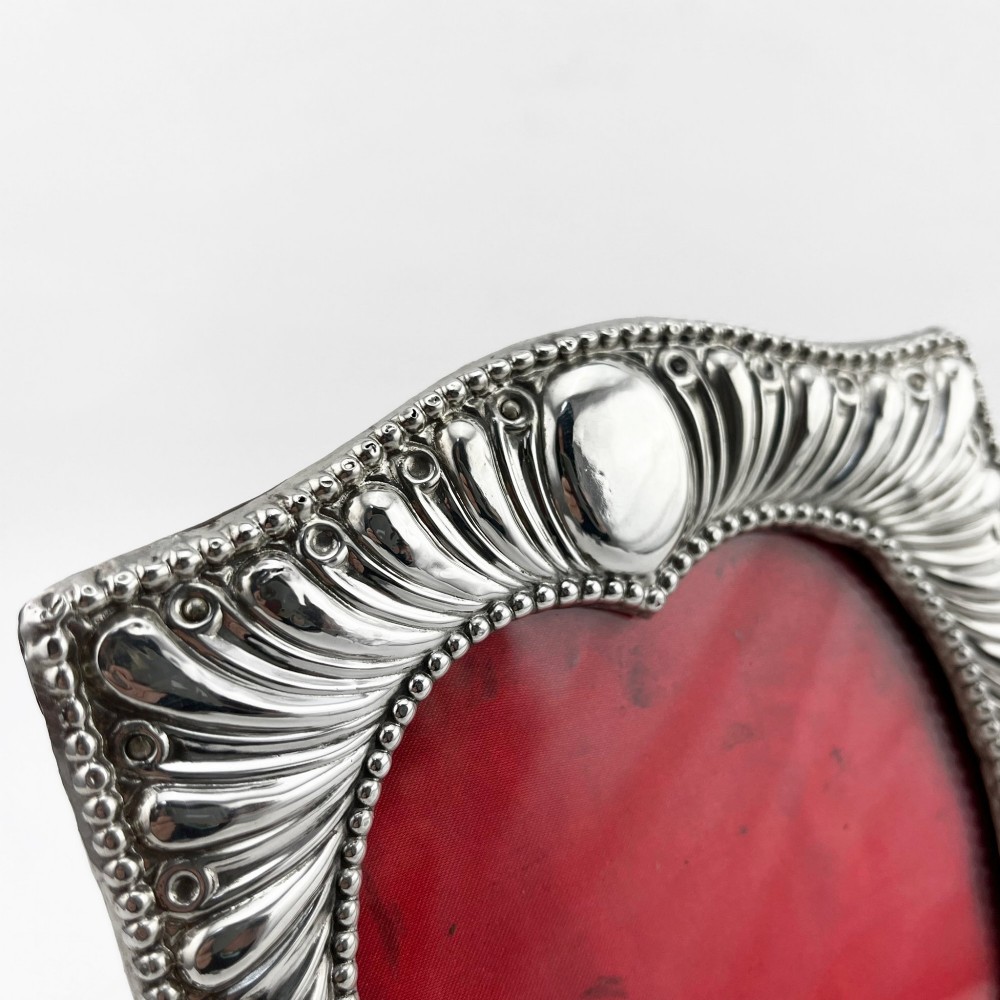 A Victorian sterling silver photo frame featuring repousse fluted patterns, a beaded border, and a heart-shaped picture aperture with a red fabric interior. View IV