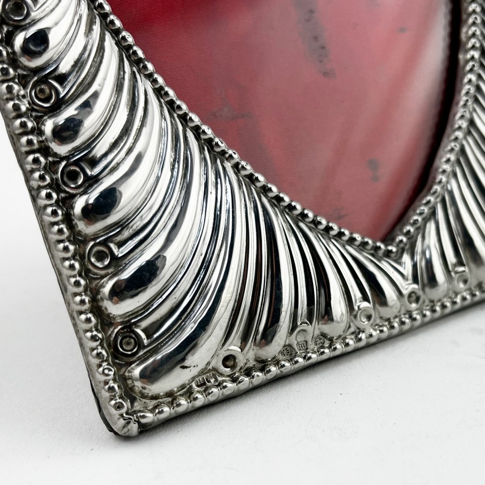 A Victorian sterling silver photo frame featuring repousse fluted patterns, a beaded border, and a heart-shaped picture aperture with a red fabric interior. View V