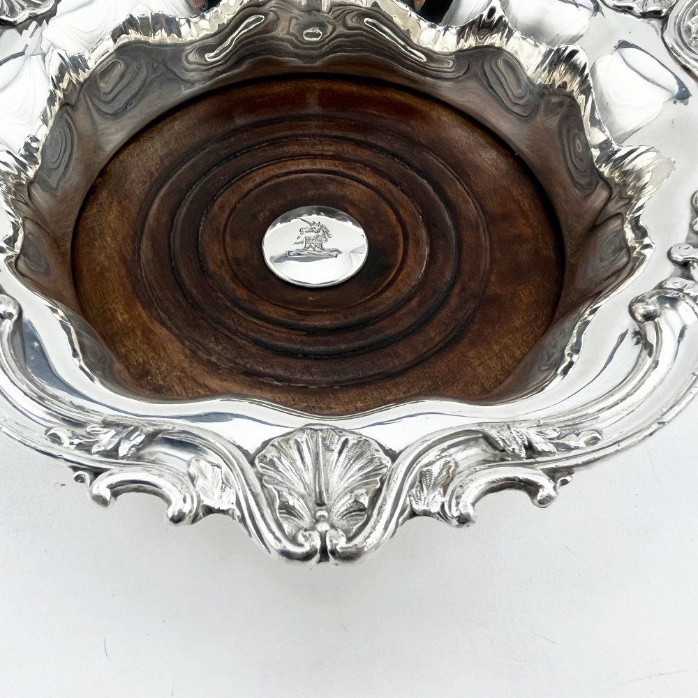 A pair of circular silver plated wine coasters featuring shell and scroll borders with turned dark wood bases and silver central bosses. View III