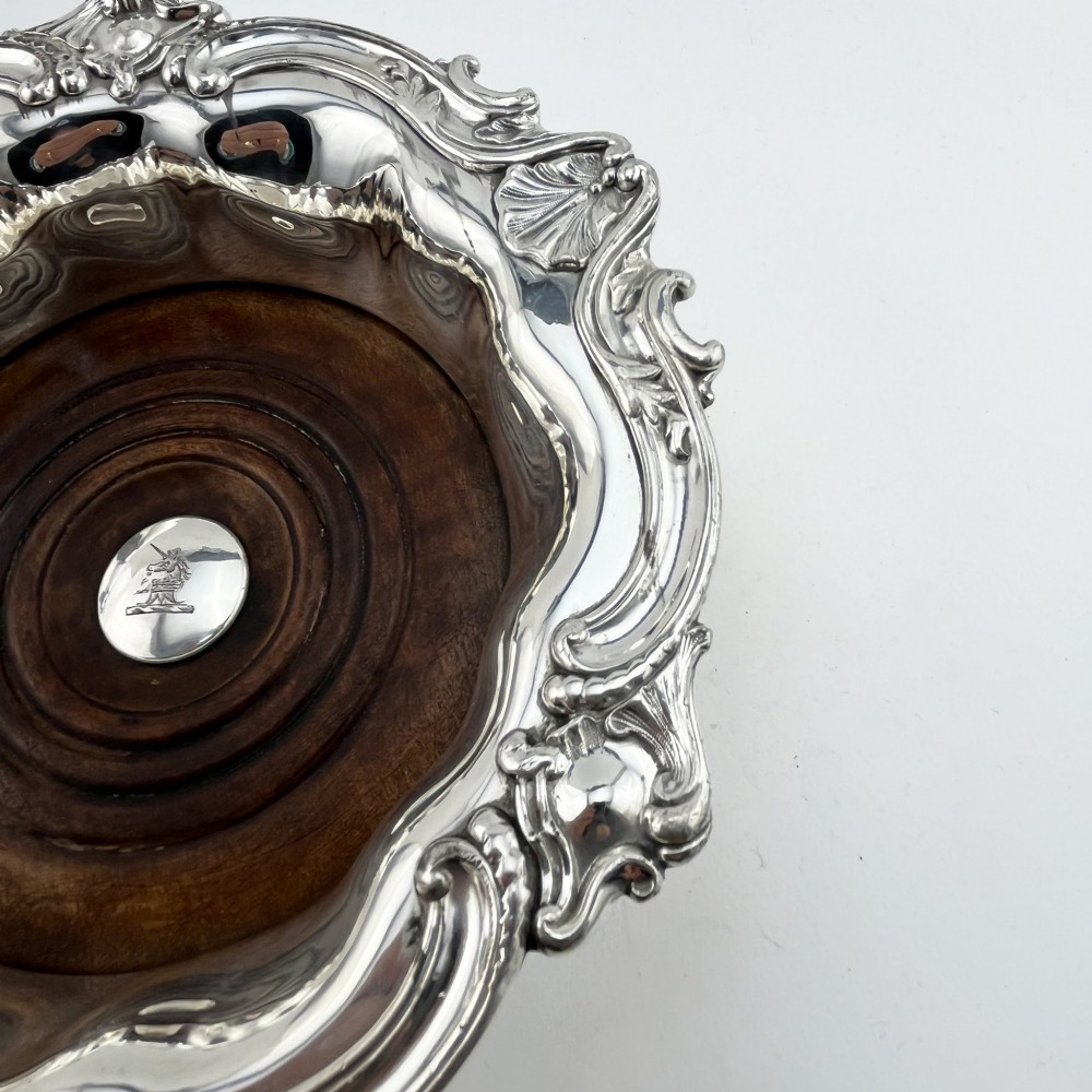 A pair of circular silver plated wine coasters featuring shell and scroll borders with turned dark wood bases and silver central bosses. View IV
