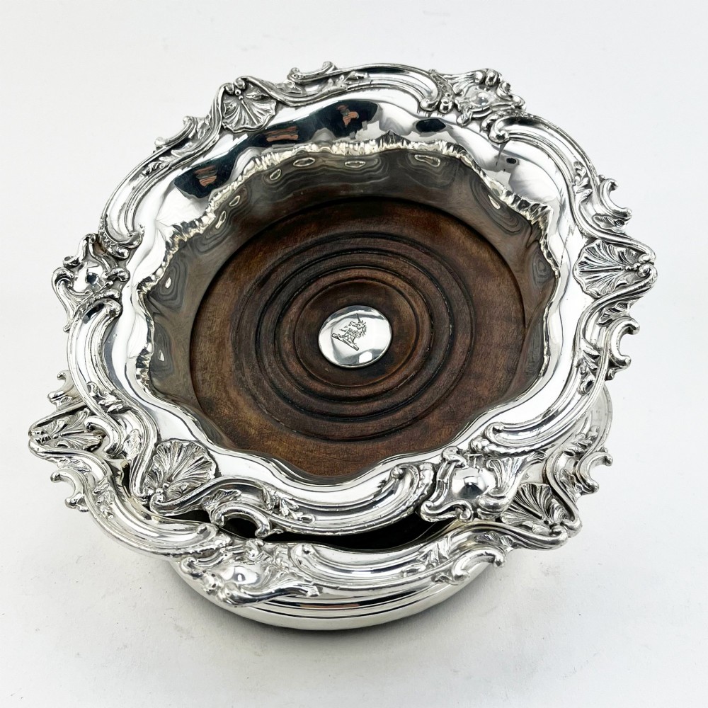 A pair of circular silver plated wine coasters featuring shell and scroll borders with turned dark wood bases and silver central bosses. View VII