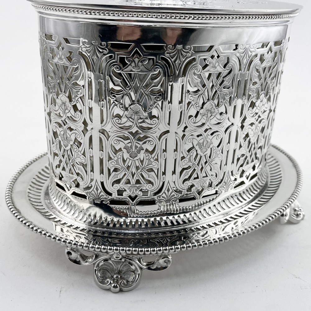 An oval Victorian silver-plated biscuit box featuring reticulated fretwork sides, an engraved lid with a dog finial, and a beaded footed base. View III