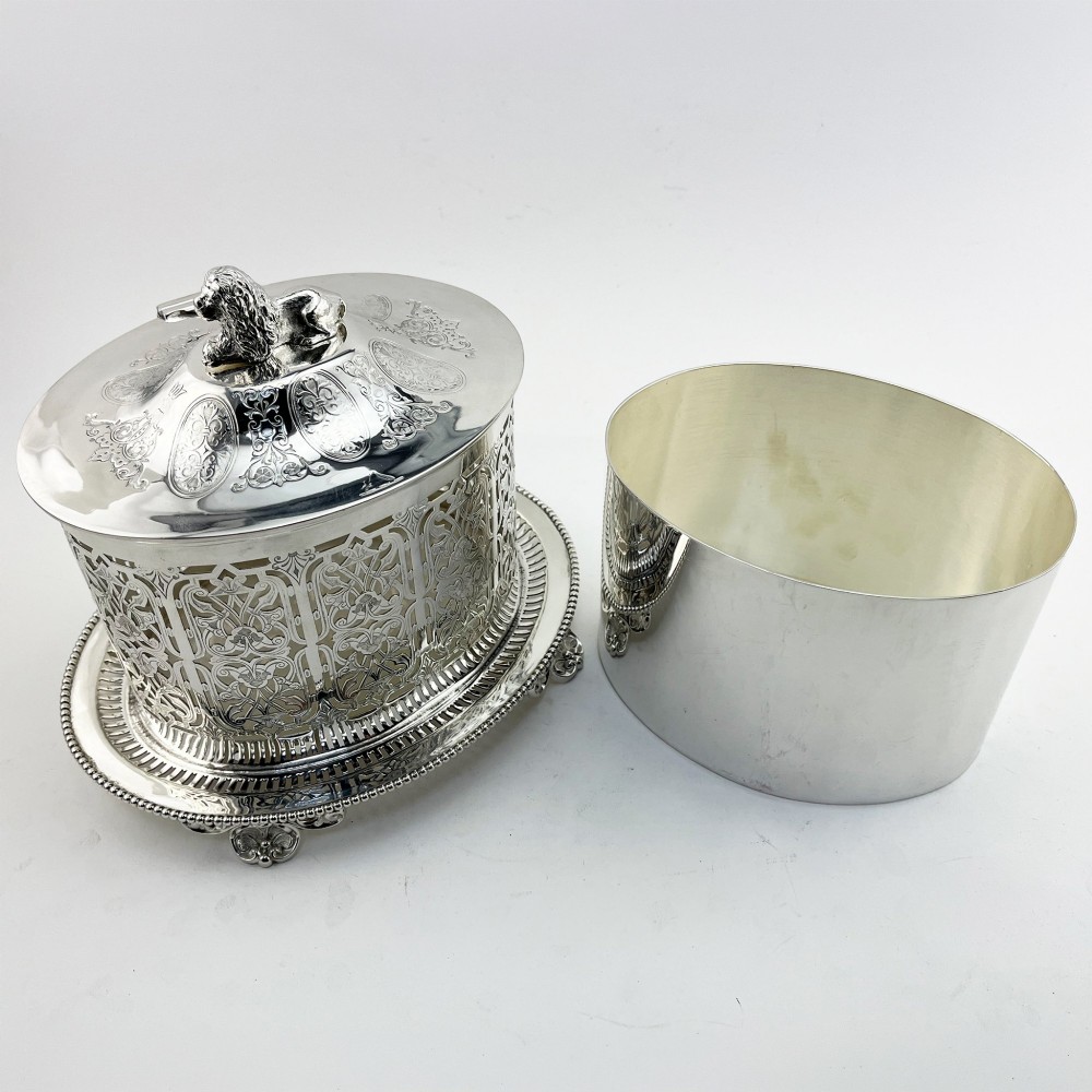 An oval Victorian silver-plated biscuit box featuring reticulated fretwork sides, an engraved lid with a dog finial, and a beaded footed base. View IV