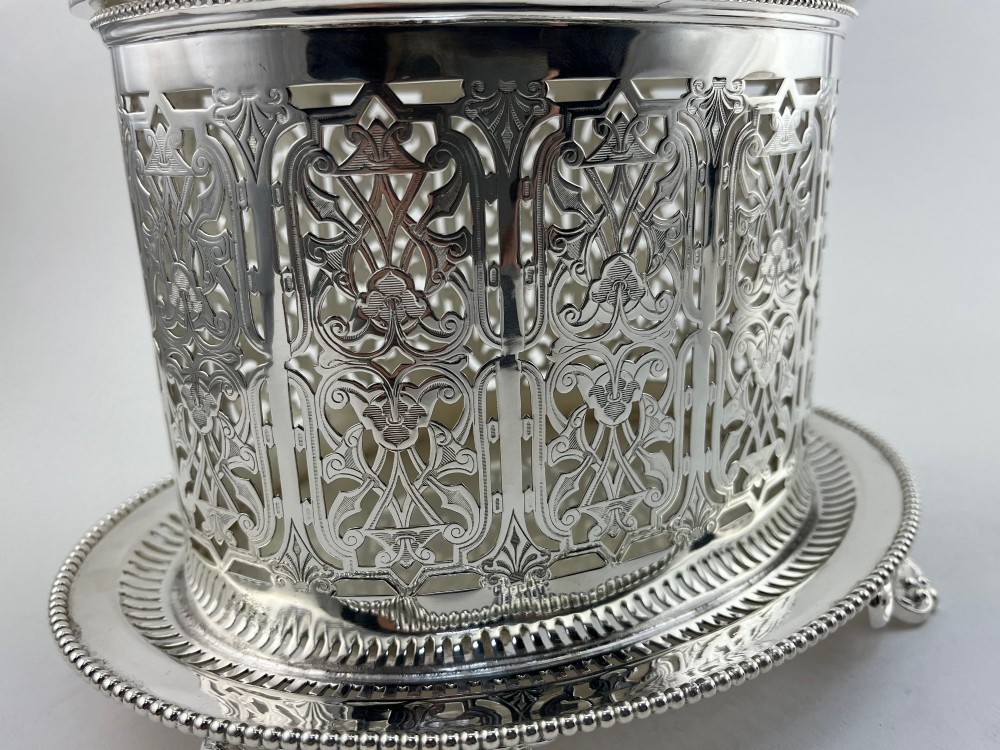 An oval Victorian silver-plated biscuit box featuring reticulated fretwork sides, an engraved lid with a dog finial, and a beaded footed base. View V