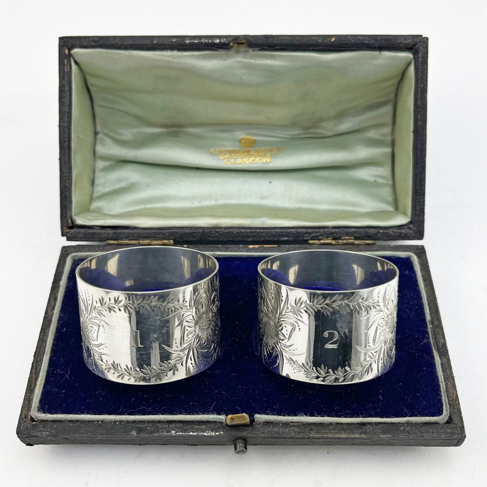 A pair of engraved Victorian sterling silver napkin rings numbered 1 and 2 inside a fitted velvet display case.
