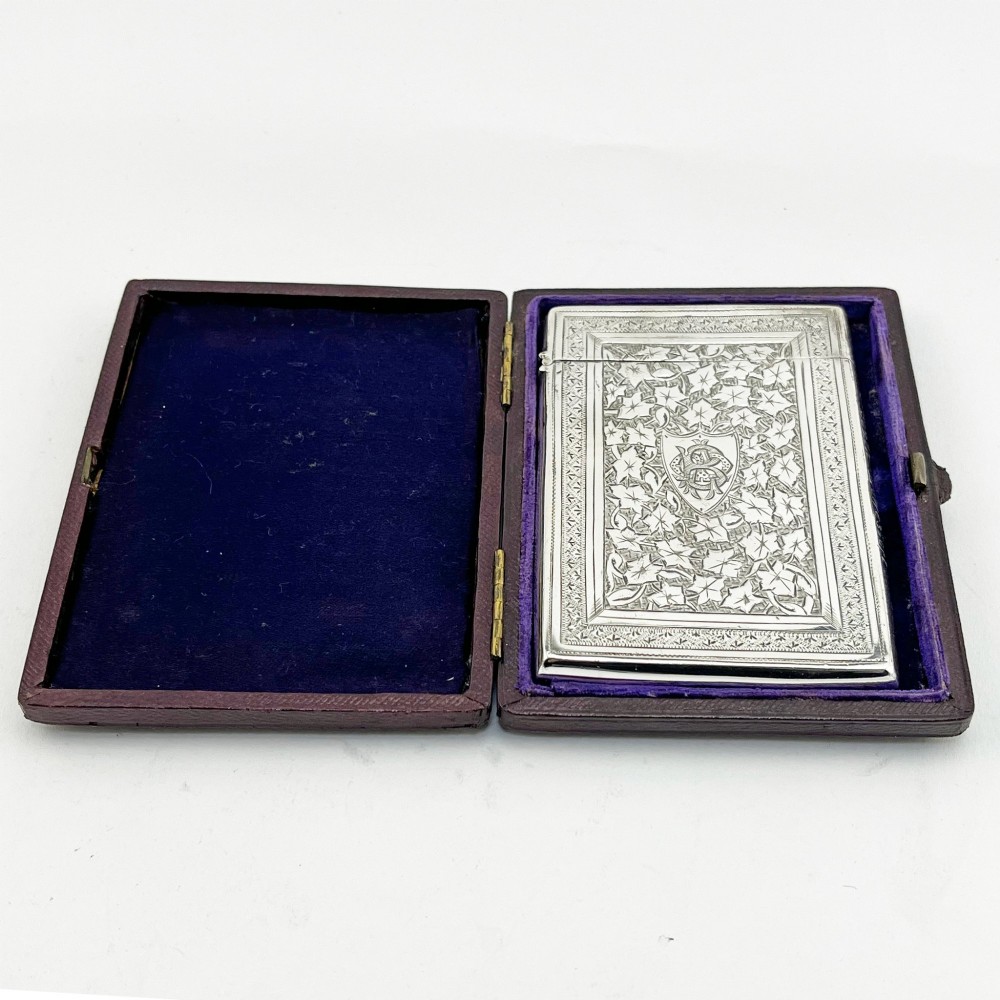 An engraved Victorian sterling silver visiting card case with ivy foliage patterning, seated inside a purple velvet-lined presentation box.