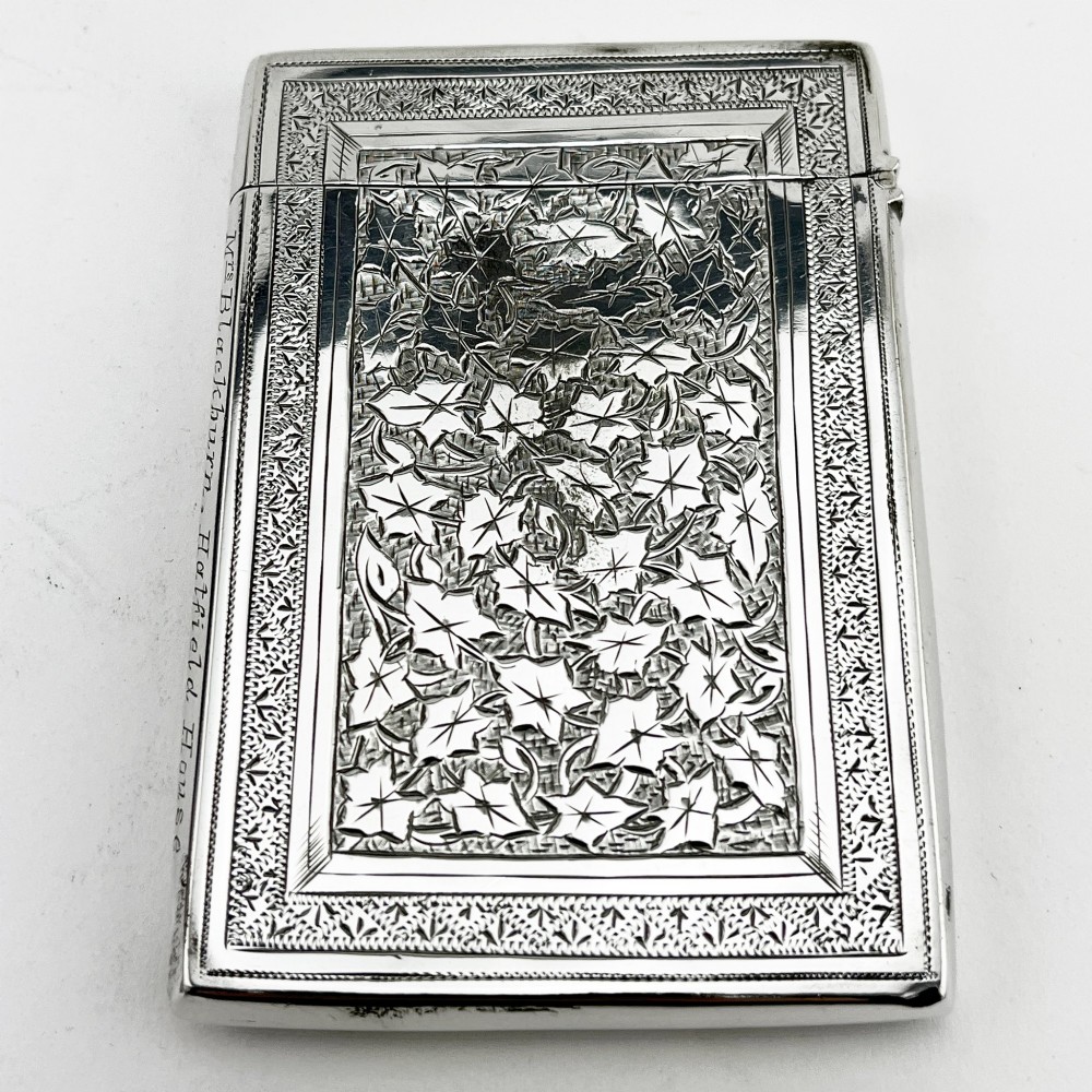 An engraved Victorian sterling silver visiting card case with ivy foliage patterning, seated inside a purple velvet-lined presentation box. View III