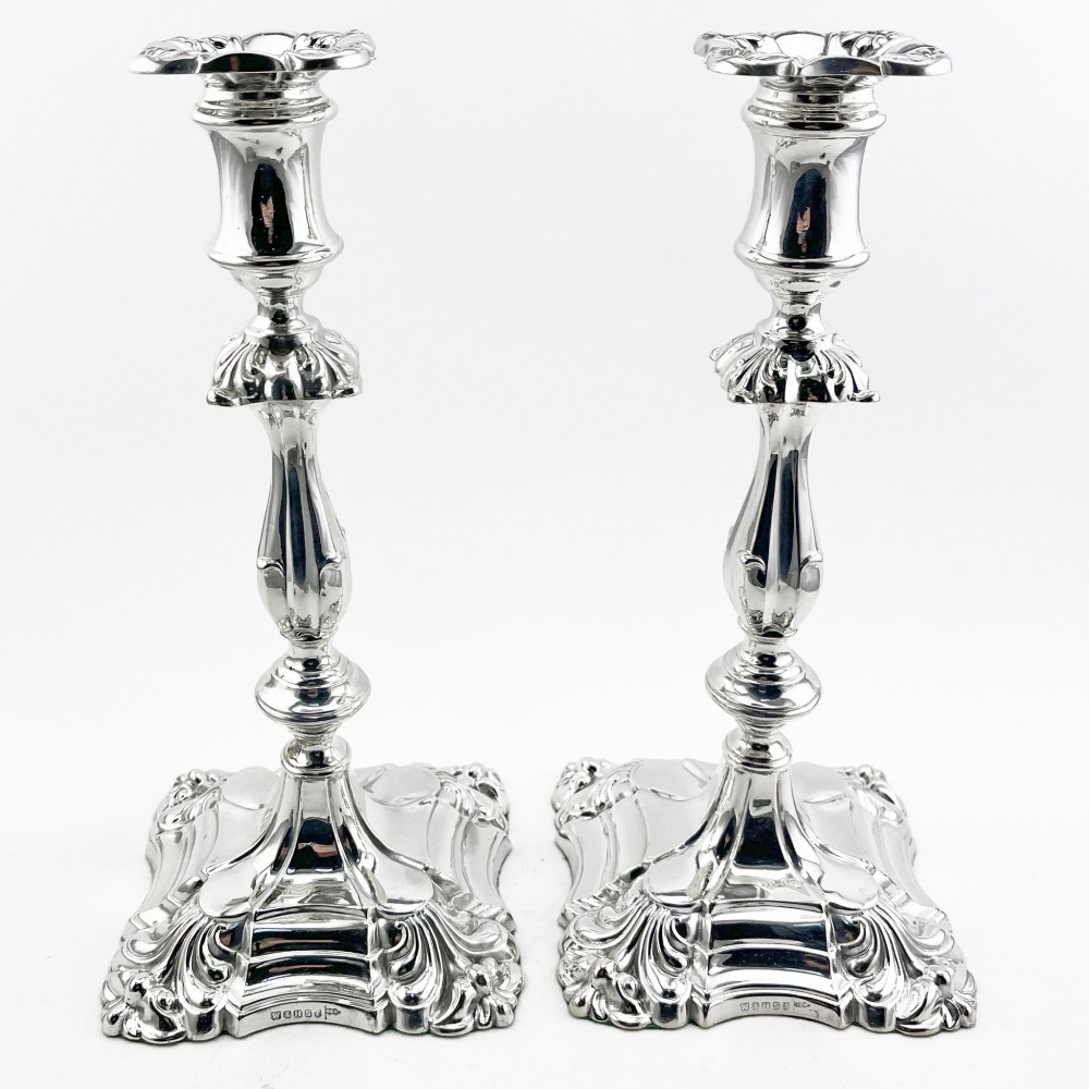 A pair of Victorian silver-plated candlesticks featuring acanthus leaf relief carving, knopped stems, and scalloped square bases.