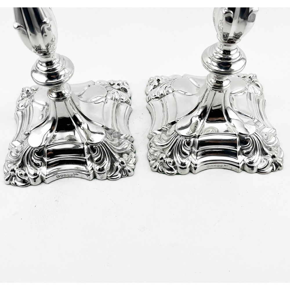 A pair of Victorian silver-plated candlesticks featuring acanthus leaf relief carving, knopped stems, and scalloped square bases. View V