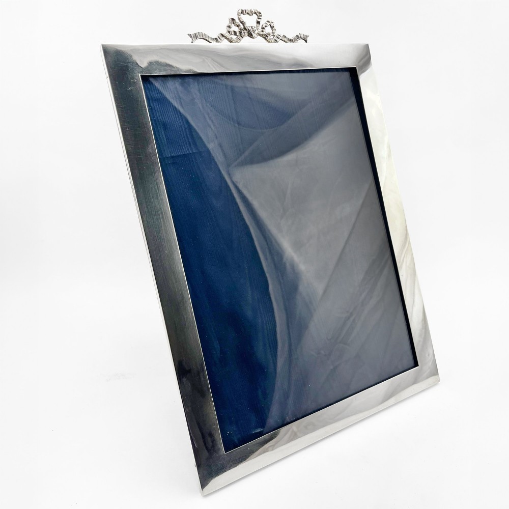 A large rectangular sterling silver photo frame with a polished finish and a carved ribbon bow crest at the top.