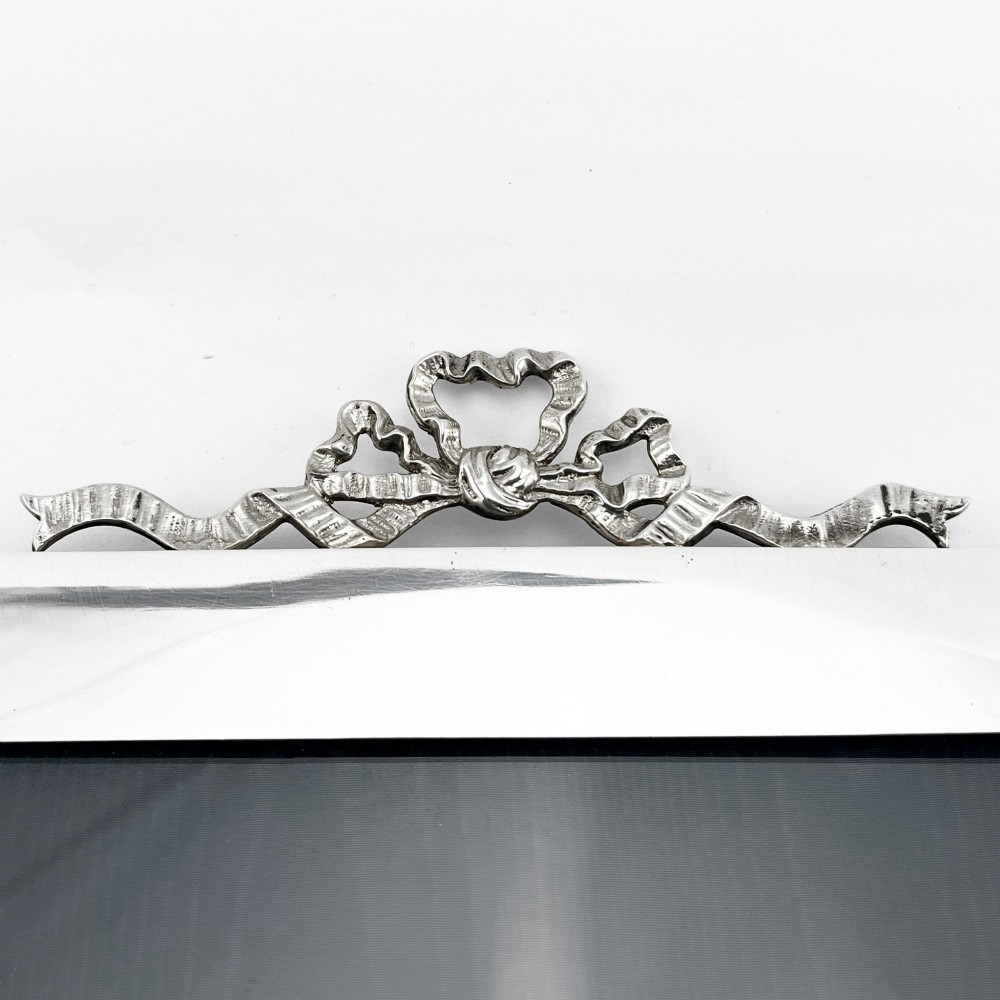 A large rectangular sterling silver photo frame with a polished finish and a carved ribbon bow crest at the top. View III