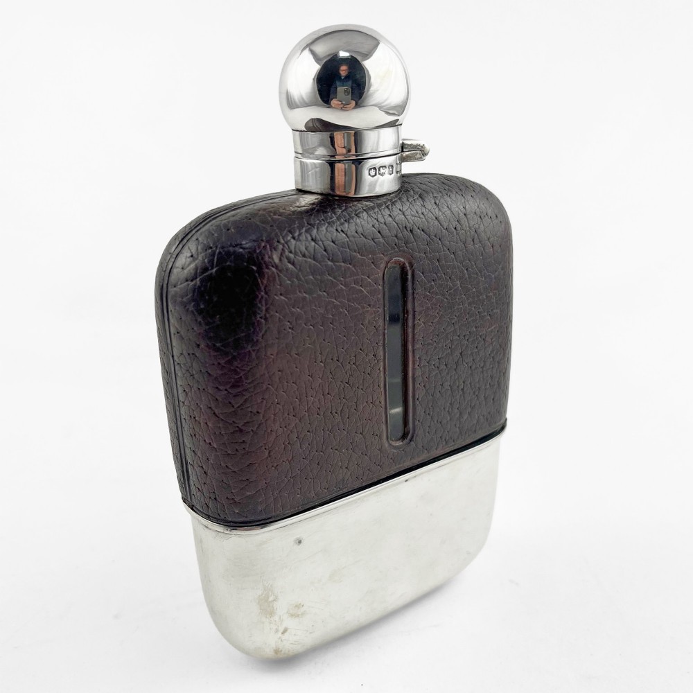 A sterling silver and textured dark brown leather hip flask with a bayonet cap, sight level window, and detachable silver base cup.
