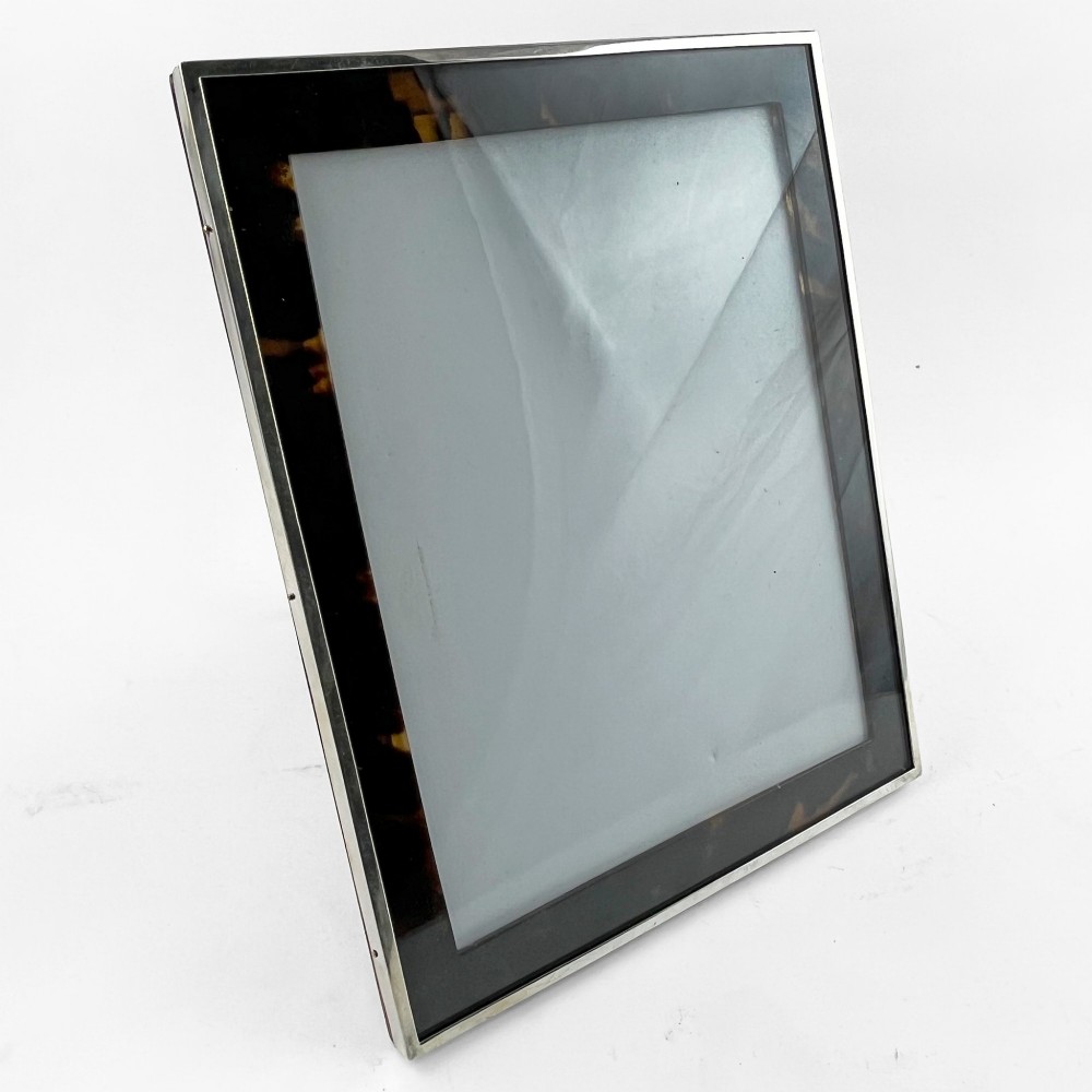 A rectangular picture frame with a mottled brown tortoiseshell border encased within a slim sterling silver outer rim.