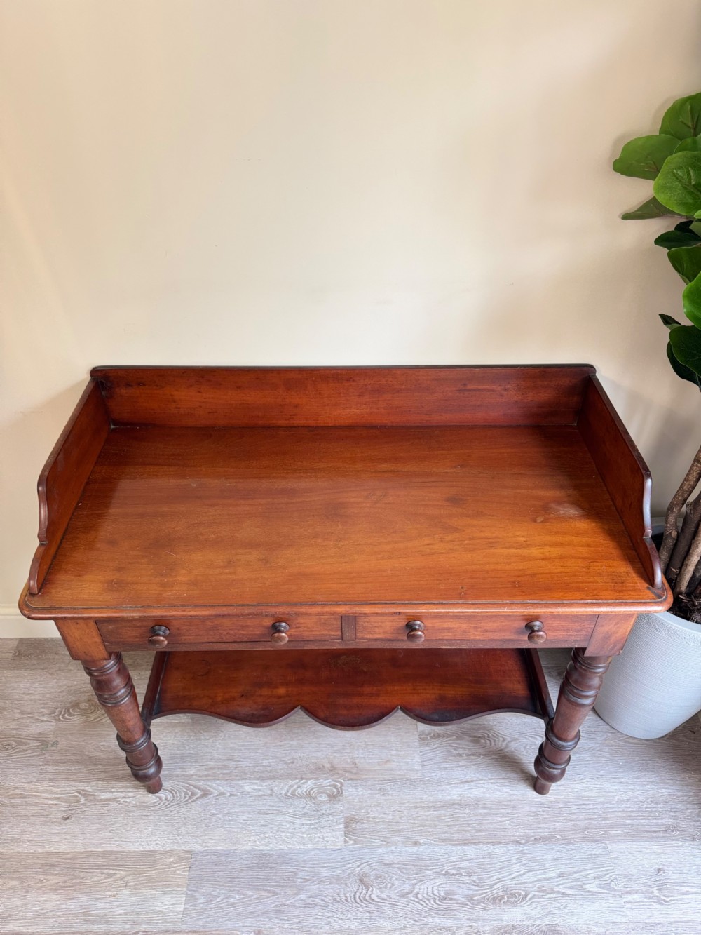 A warm brown mahogany console table featuring a rear splashback gallery, two drawers with wooden knobs, turned legs, and a shaped lower shelf. View VI