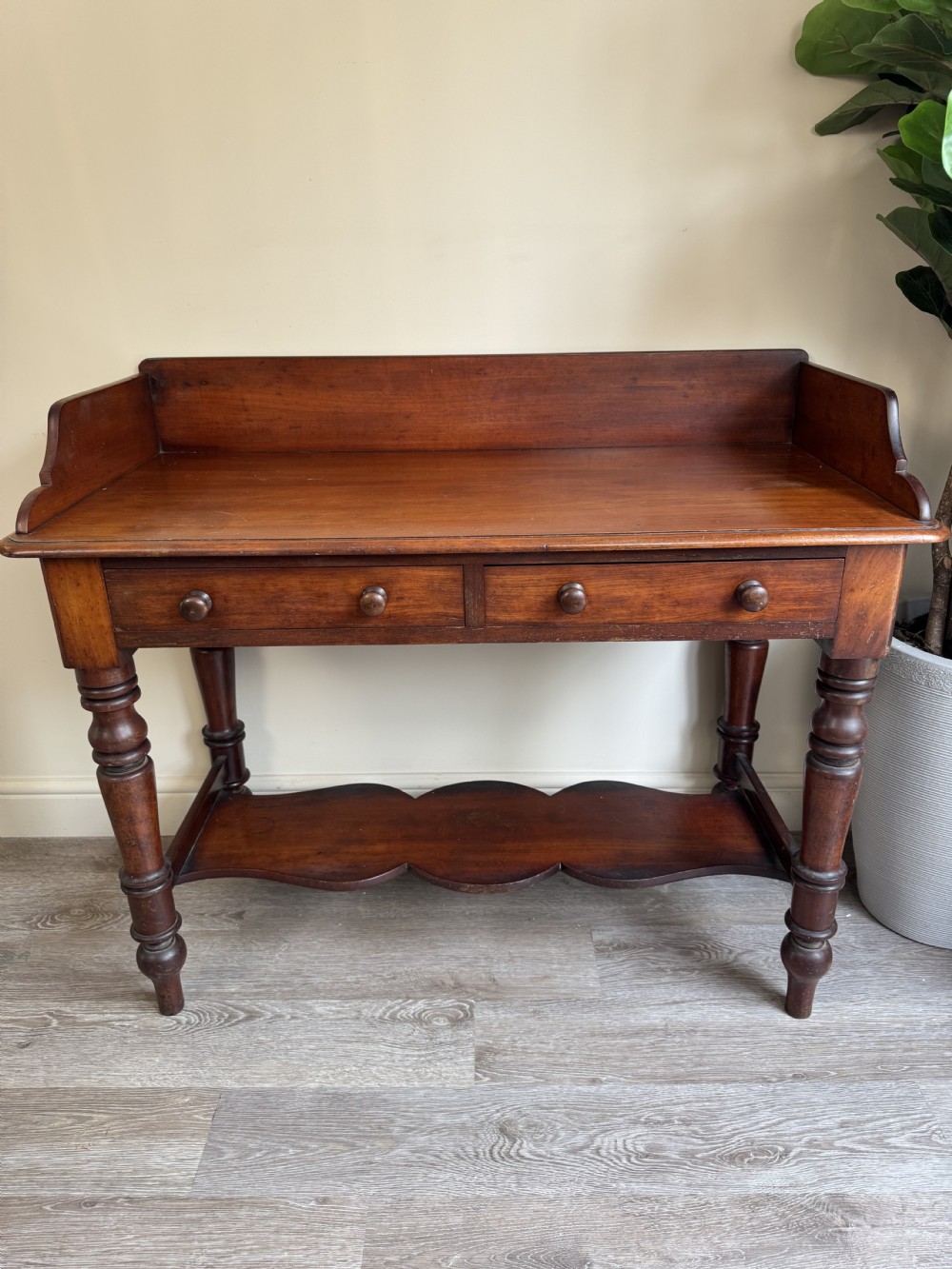 A warm brown mahogany console table featuring a rear splashback gallery, two drawers with wooden knobs, turned legs, and a shaped lower shelf. View III