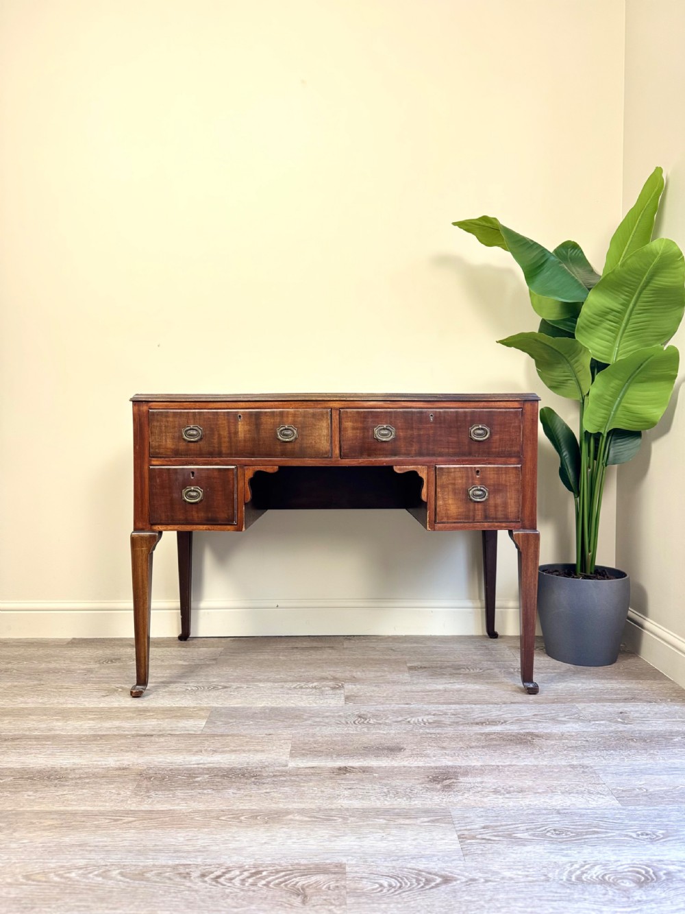 An Edwardian solid mahogany dressing table with brass drop handles, multiple drawers, a kneehole apron, and tapered legs.