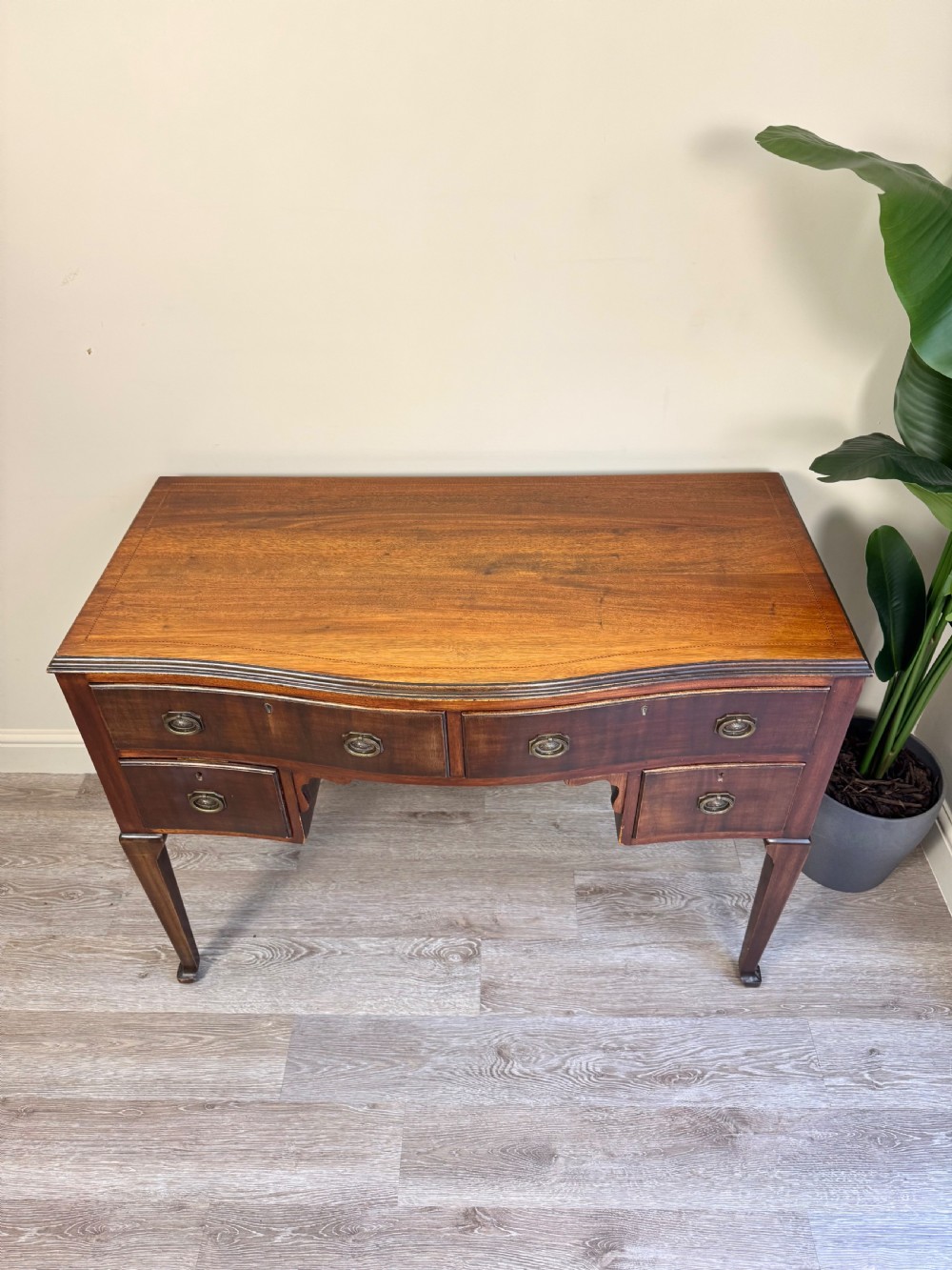An Edwardian solid mahogany dressing table with brass drop handles, multiple drawers, a kneehole apron, and tapered legs. View V