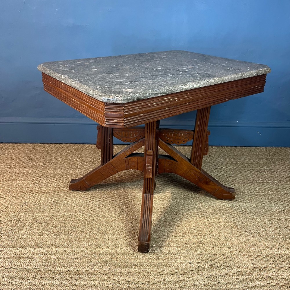 An Aesthetic Movement occasional table featuring a grey Derbyshire fossil marble top set upon an incised carved wooden base.