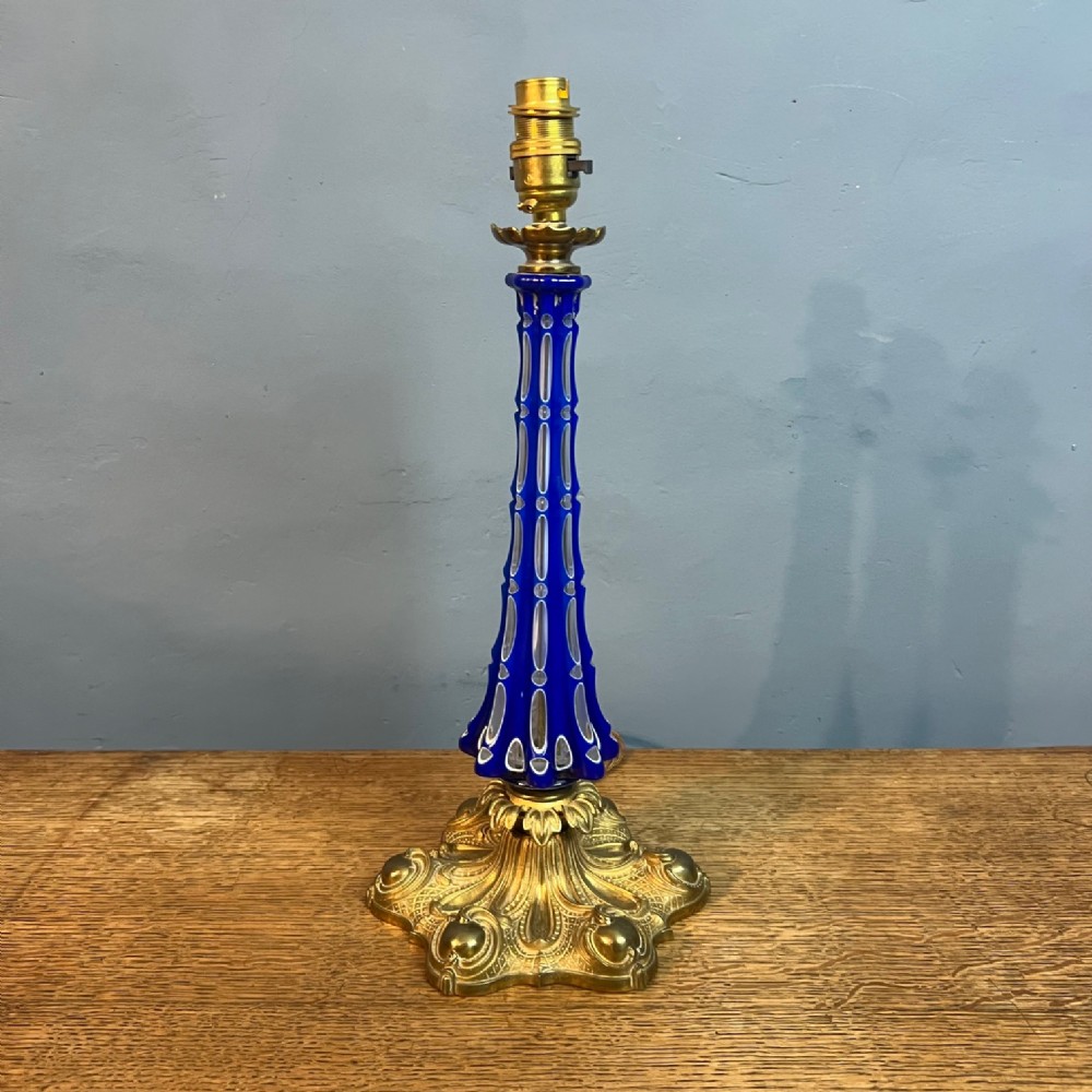 A mid-19th century table lamp featuring a tapered cobalt blue cut glass stem mounted on an ornate gilt brass rococo base.