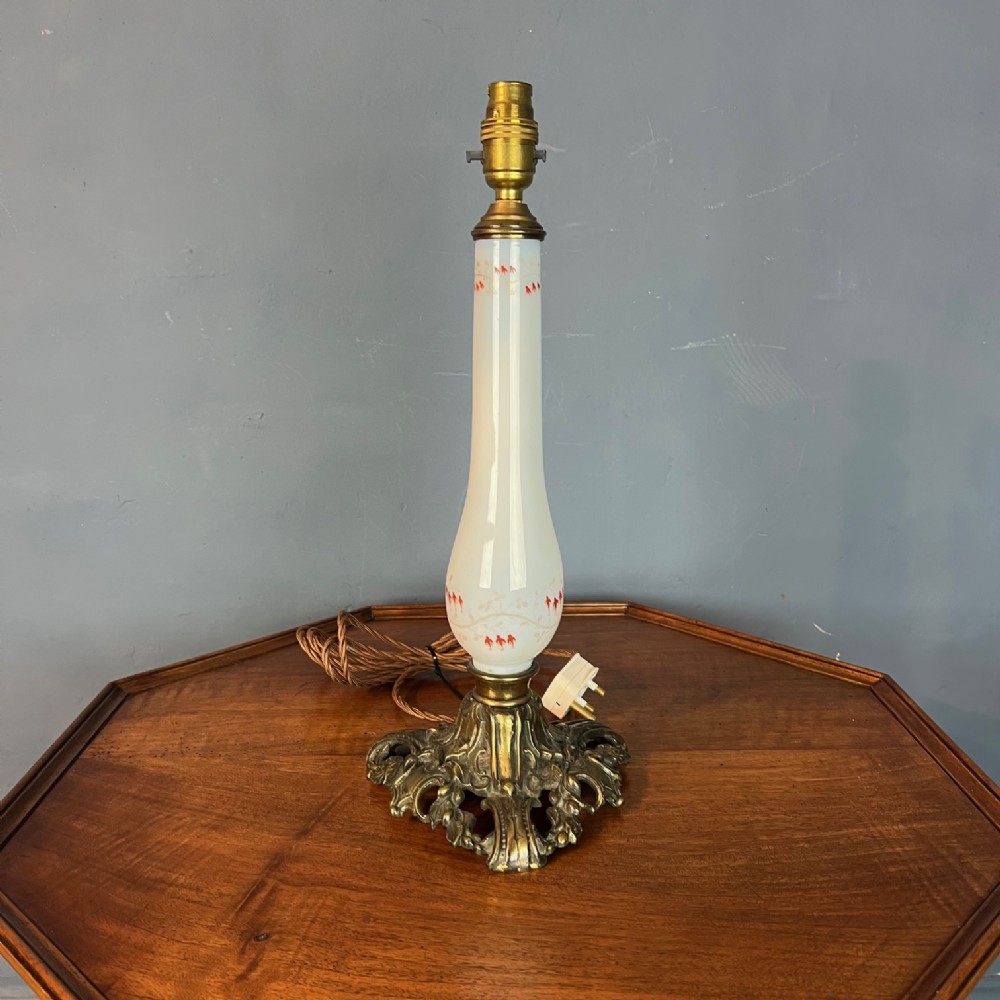 A Victorian opaline white glass table lamp base featuring hand-painted red floral detailing mounted on an ornate cast brass foot.