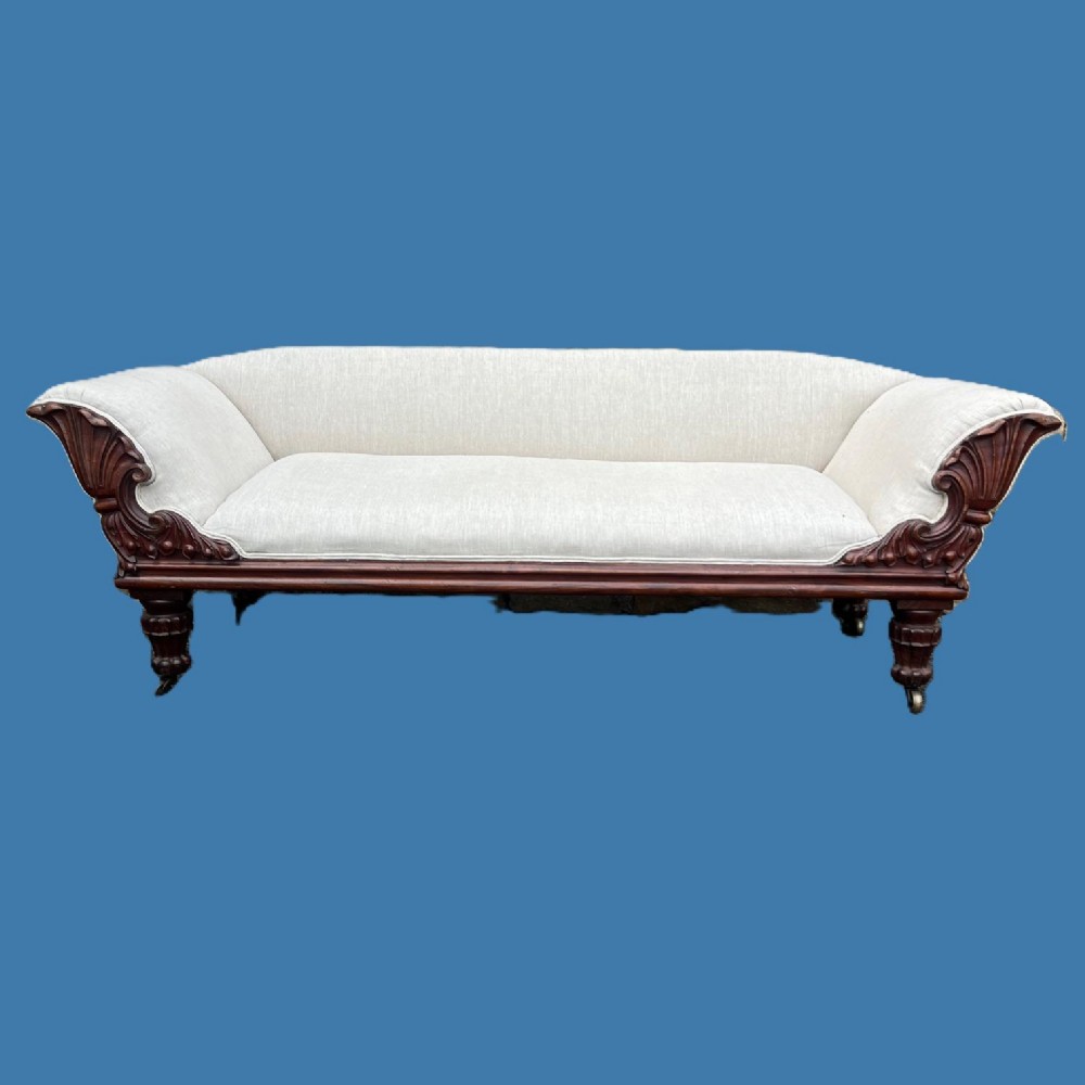 A William IV carved mahogany sofa featuring scroll arms, cream fabric upholstery, turned lobed legs, and brass castors.