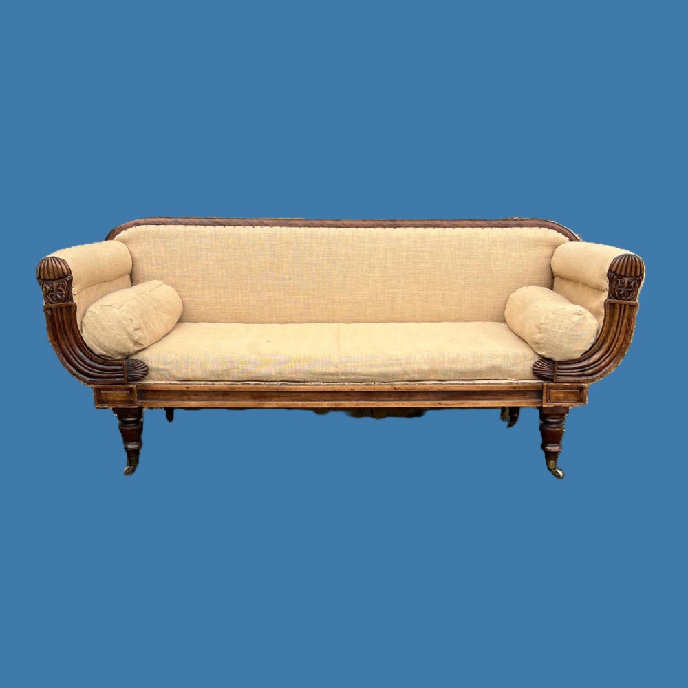 A George IV simulated rosewood campaign sofa with carved scroll arms, bolster cushions, neutral upholstery, turned reeded legs, and brass castors.