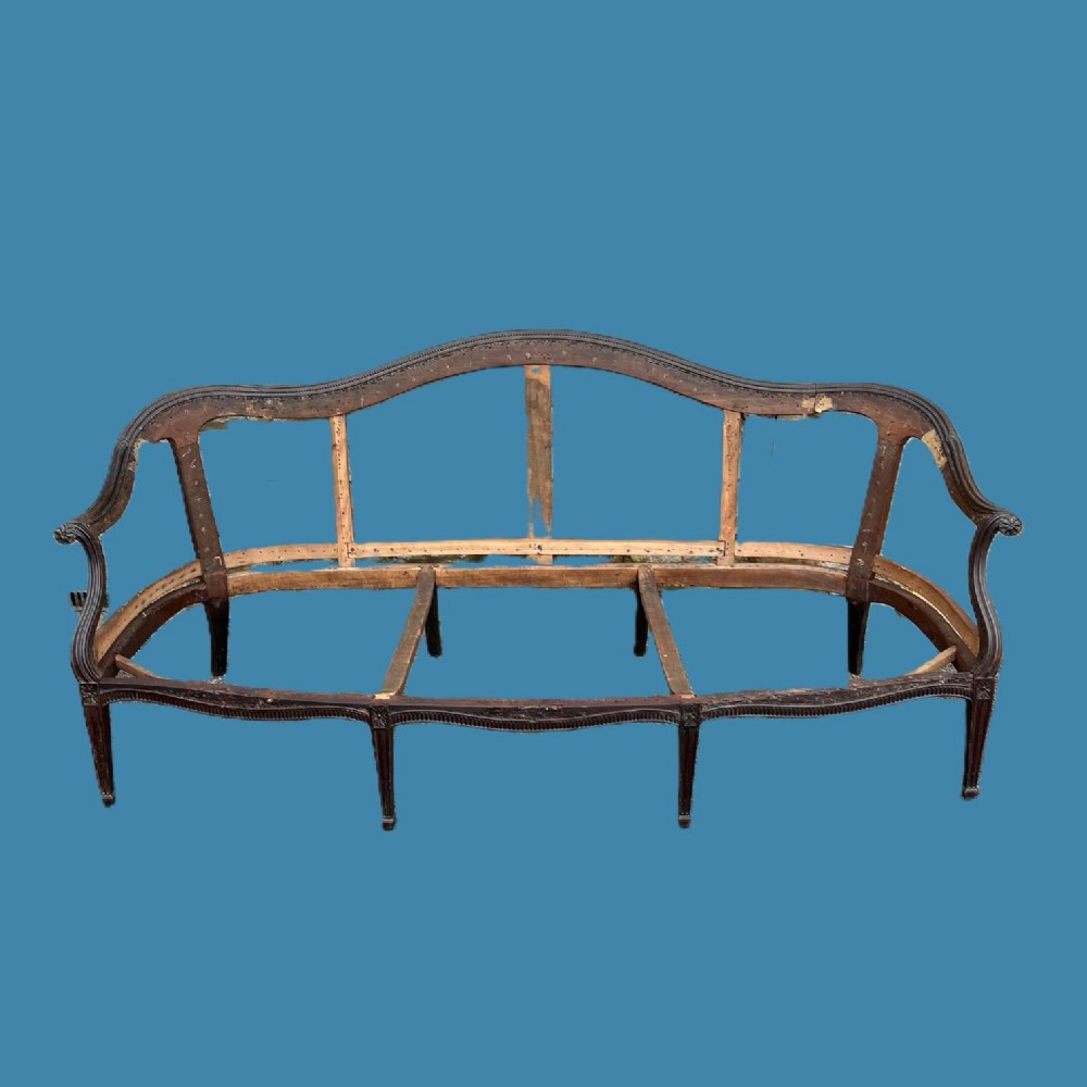 An un-upholstered carved mahogany sofa frame from the George III period featuring a serpentine crest rail and tapered carved legs.