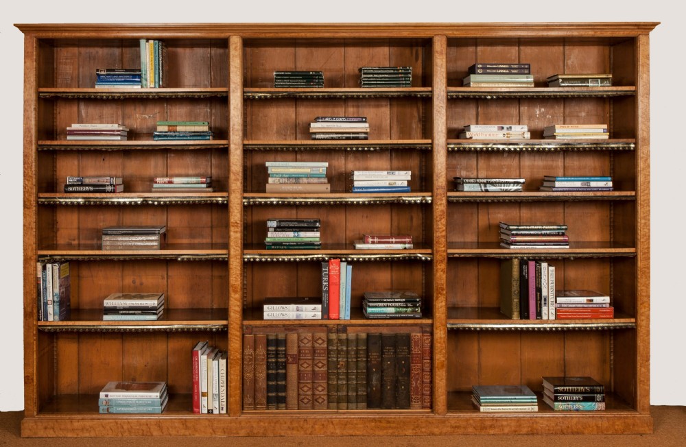 A large nineteenth-century open-front birdseye maple bookcase featuring three vertical sections, adjustable shelves with leather dust aprons, and a lower concealed compartment holding books. View II