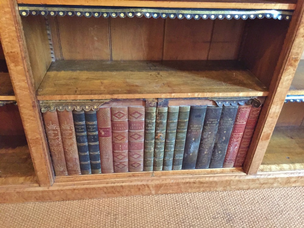 A large nineteenth-century open-front birdseye maple bookcase featuring three vertical sections, adjustable shelves with leather dust aprons, and a lower concealed compartment holding books. View IV