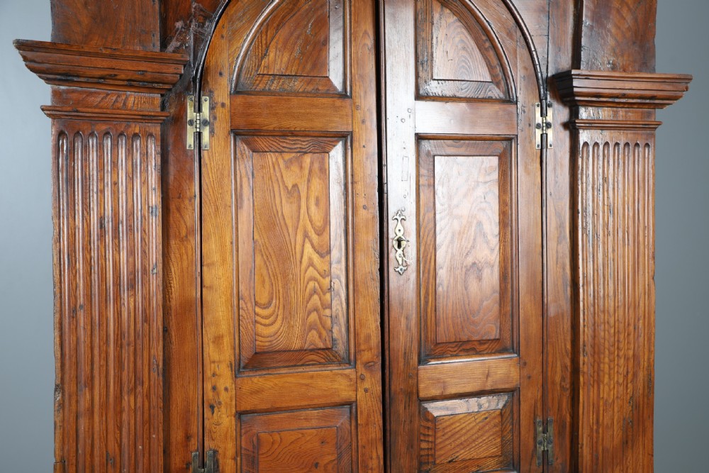 An eighteenth-century standing architectural corner cupboard made of warm brown elm timber with arched panel doors, fluted side pilasters, and a moulded cornice. View II