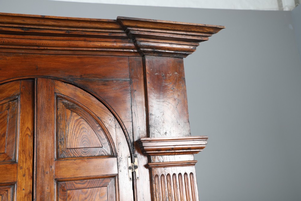 An eighteenth-century standing architectural corner cupboard made of warm brown elm timber with arched panel doors, fluted side pilasters, and a moulded cornice. View III