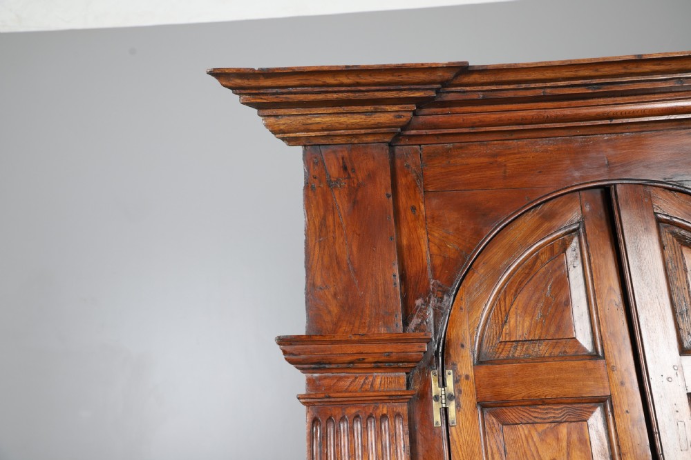 An eighteenth-century standing architectural corner cupboard made of warm brown elm timber with arched panel doors, fluted side pilasters, and a moulded cornice. View IV