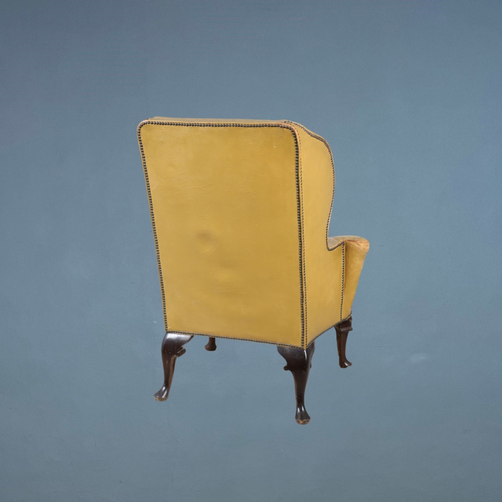 Late 19th-century wingback armchair upholstered in aged tan leather featuring high side wings, brass studding, and dark wooden cabriole legs. View II