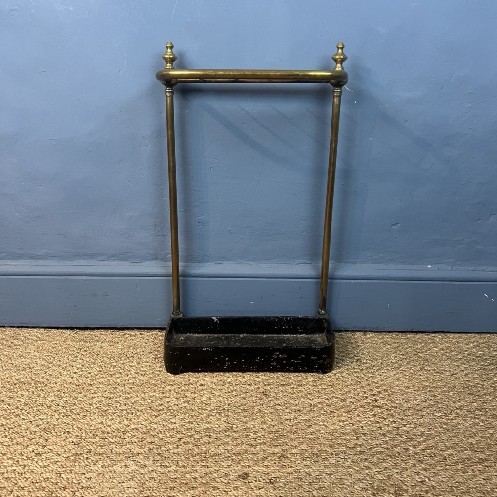 A late 19th-century brass tubular stick stand featuring urn finials and a black cast-iron drip tray base.