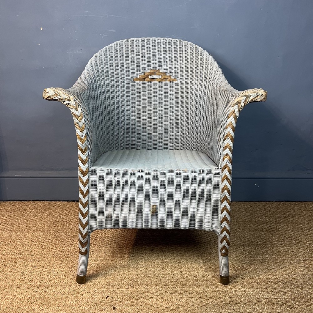 A 1931 woven Lloyd Loom armchair in light blue with gold braided trim along the flared armrests and a geometric backrest motif.