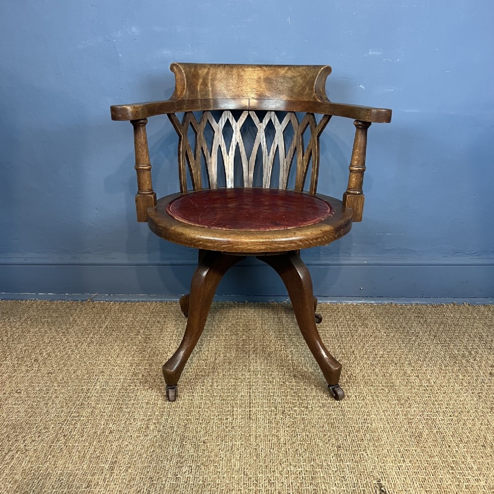 A late Victorian revolving oak desk chair featuring a curved backrest with lattice carving, turned arm supports, a red leather circular seat, and swept legs with castors.