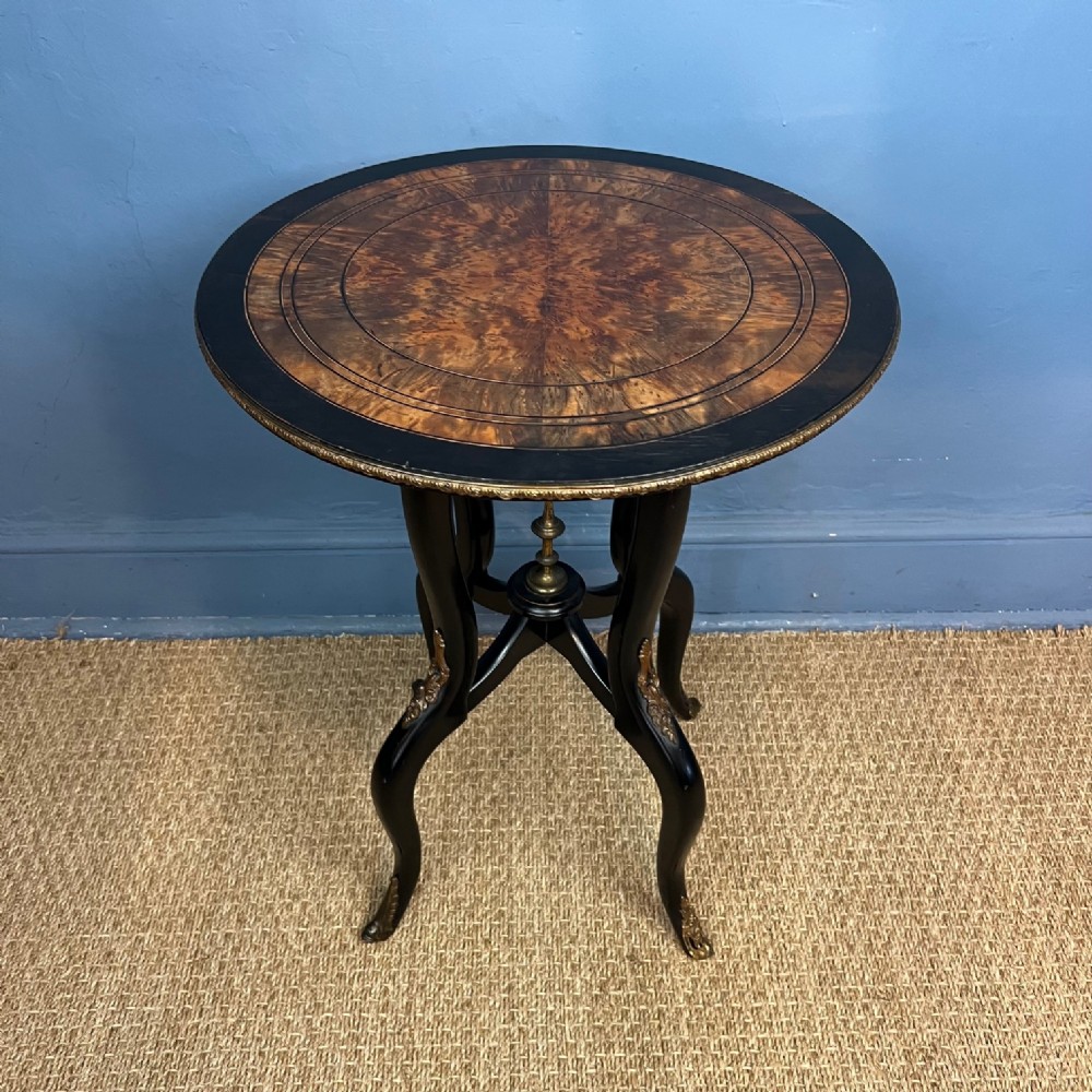 A circular late 19th-century occasional table featuring a central thuyawood burr inlay surrounded by an ebonised border with carved legs and brass mounts.
